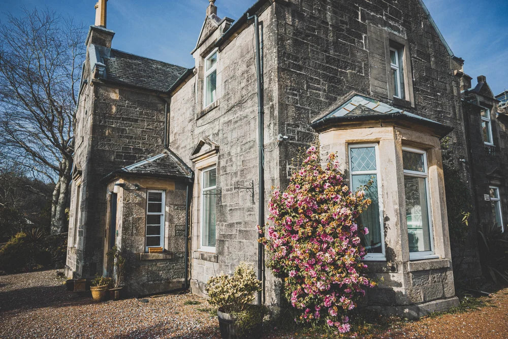 Heatherfield  House in Oban with a flowering bush in front on a clear day